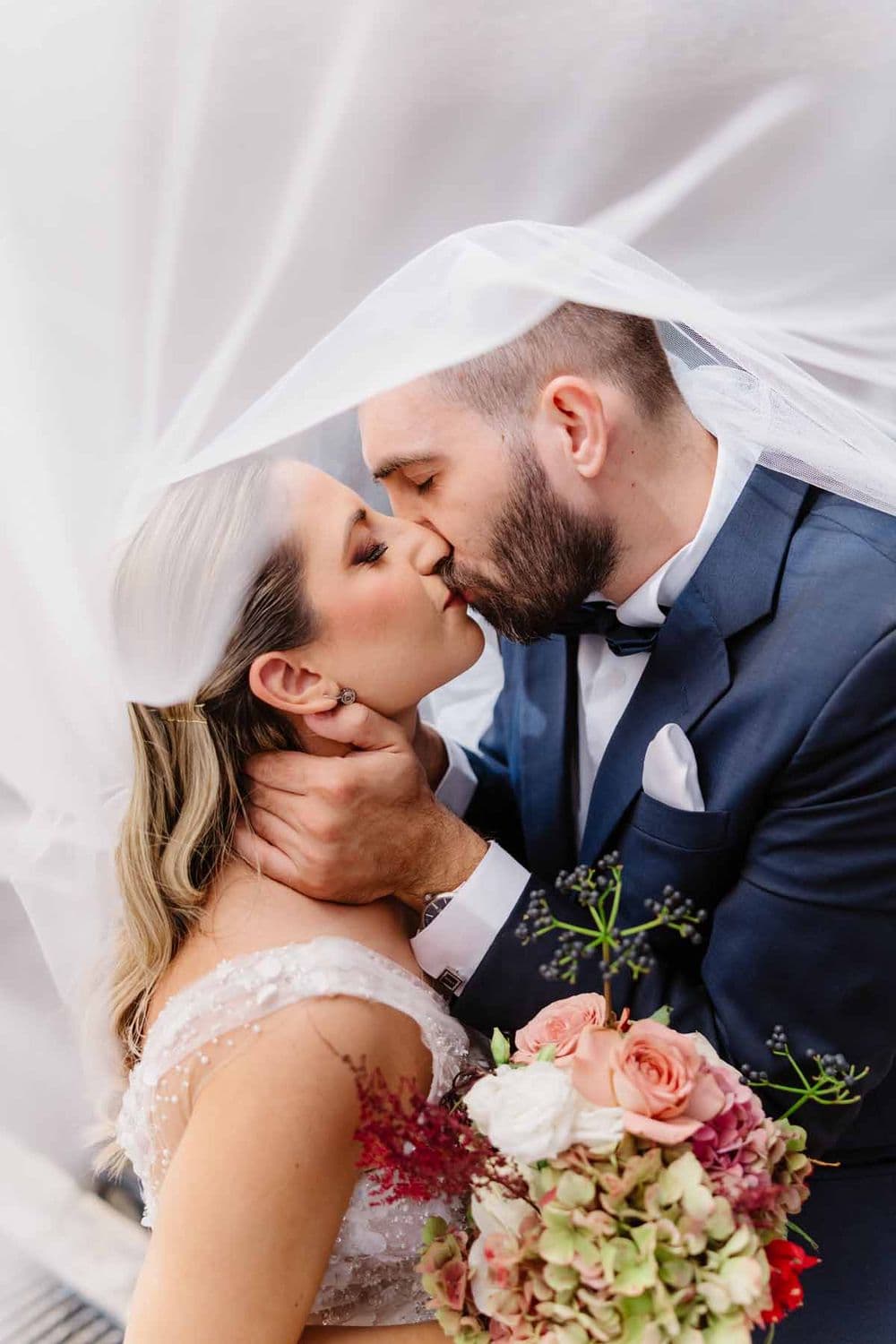 Bride and groom kissing under a flowing veil