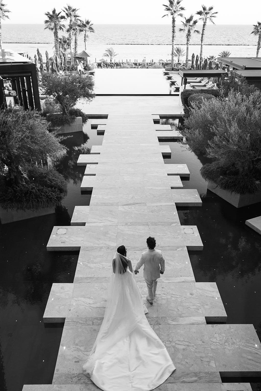 Bride and groom walking across the water garden, in black and white